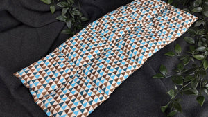 Körnerkissen mit blauen, brauen und türkisfarbenen Dreiecken auf beigem Hintergrund