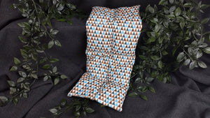 Körnerkissen mit blauen, brauen und türkisfarbenen Dreiecken auf beigem Hintergrund