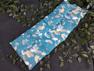 Körnerkissen mit blauem Hintergrund und petrolfarbenen und beige/weißen Ginkgoblättern im Vordergrund