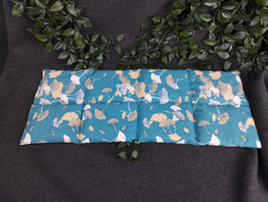 Körnerkissen mit blauem Hintergrund und petrolfarbenen und beige/weißen Ginkgoblättern im Vordergrund