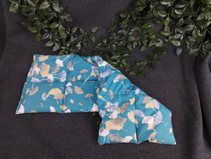 Körnerkissen mit blauem Hintergrund und petrolfarbenen und beige/weißen Ginkgoblättern im Vordergrund