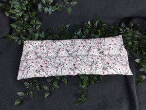 Gesamtaufnahme unseres 50x20cm großen, in 8 Kammern unterteiltes Körnerkissen mit Kirschblütenmotiv. Es zeigt eine Vielzahl an aufgehenden Kirschblüten. Der Hintergrund ist in einem dezenten hellgrau gehalten. Darauf abgebildet sind Äste des Kirschbaums, der im Anfang seiner Blüte steht. Viele der Triebe sind schon geöffnet und zeigen die Schönheit der Kirschblüte. Die Blütenblätter sind weiß bis hellrosa, wo hingegen der Blütenstempel in schwarz und einem dunklem Beerenton gehalten ist.