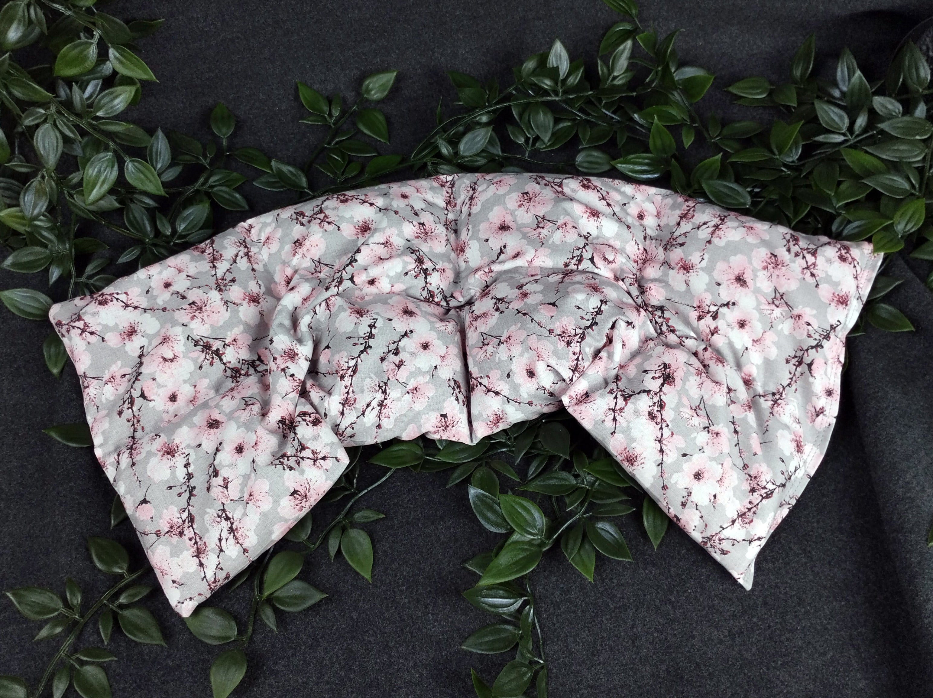 Unser Körnerkissen Kirschblüte ist im Bogen hingelegt. Es zeigt eine Vielzahl an aufgehenden Kirschblüten. Der Hintergrund ist in einem dezenten hellgrau gehalten. Darauf abgebildet sind Äste des Kirschbaums, der im Anfang seiner Blüte steht. Viele der Triebe sind schon geöffnet und zeigen die Schönheit der Kirschblüte. Die Blütenblätter sind weiß bis hellrosa, wo hingegen der Blütenstempel in schwarz und einem dunklem Beerenton gehalten ist.