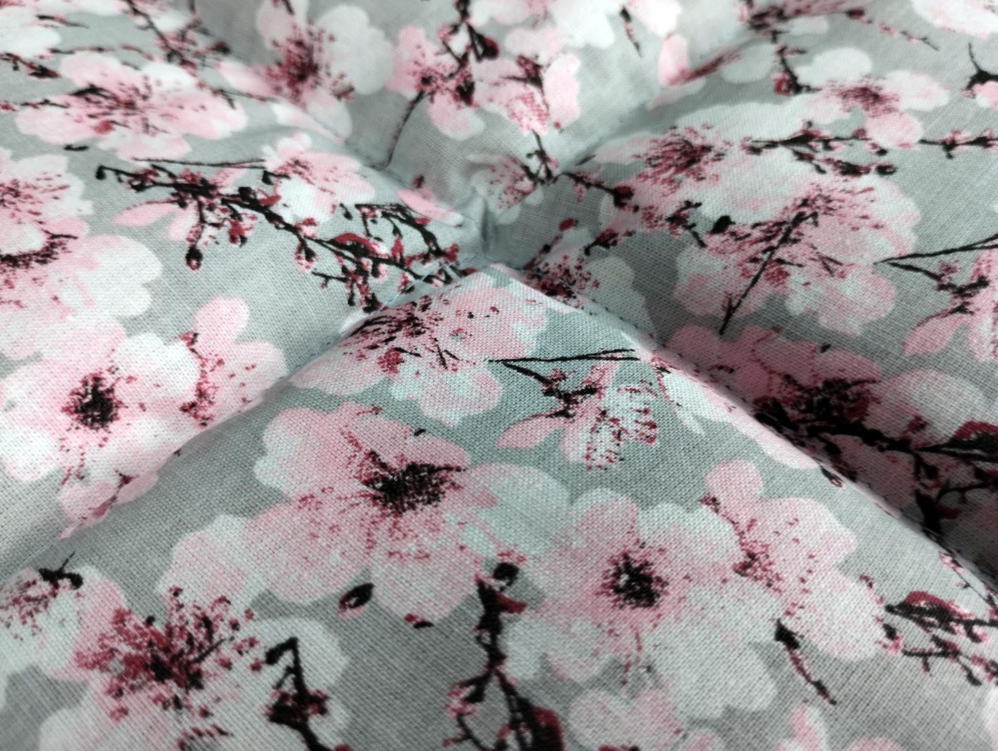 Nahaufnahme von unserm Körnerkissen Kirschblüte. Es zeigt eine Vielzahl an aufgehenden Kirschblüten. Der Hintergrund ist in einem dezenten hellgrau gehalten. Darauf abgebildet sind Äste des Kirschbaums, der im Anfang seiner Blüte steht. Viele der Triebe sind schon geöffnet und zeigen die Schönheit der Kirschblüte. Die Blütenblätter sind weiß bis hellrosa, wo hingegen der Blütenstempel in schwarz und einem dunklem Beerenton gehalten ist.