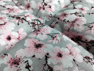 Nahaufnahme von unserm Körnerkissen Kirschblüte. Es zeigt eine Vielzahl an aufgehenden Kirschblüten. Der Hintergrund ist in einem dezenten hellgrau gehalten. Darauf abgebildet sind Äste des Kirschbaums, der im Anfang seiner Blüte steht. Viele der Triebe sind schon geöffnet und zeigen die Schönheit der Kirschblüte. Die Blütenblätter sind weiß bis hellrosa, wo hingegen der Blütenstempel in schwarz und einem dunklem Beerenton gehalten ist.