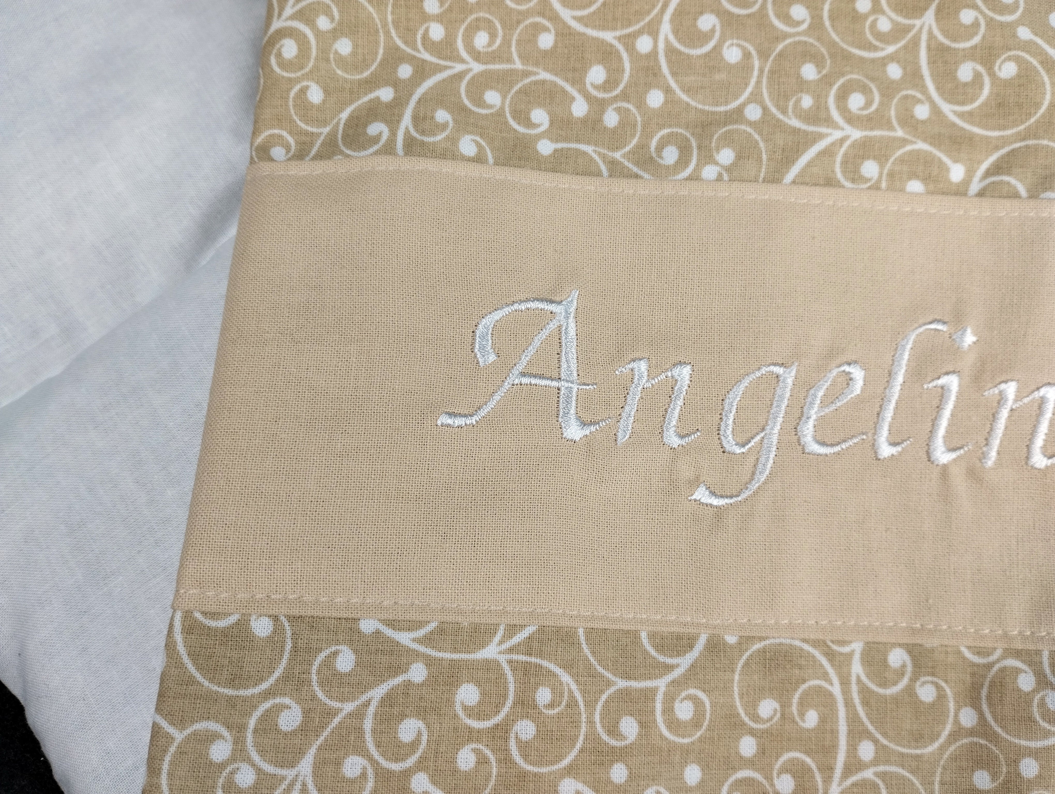 personalisiertes Körnerkissen mit dem Namen Angelina. Das Hauptmotiv in beige mit weißen Ranken und der Name weiß gestickt auf beigem Stoff.