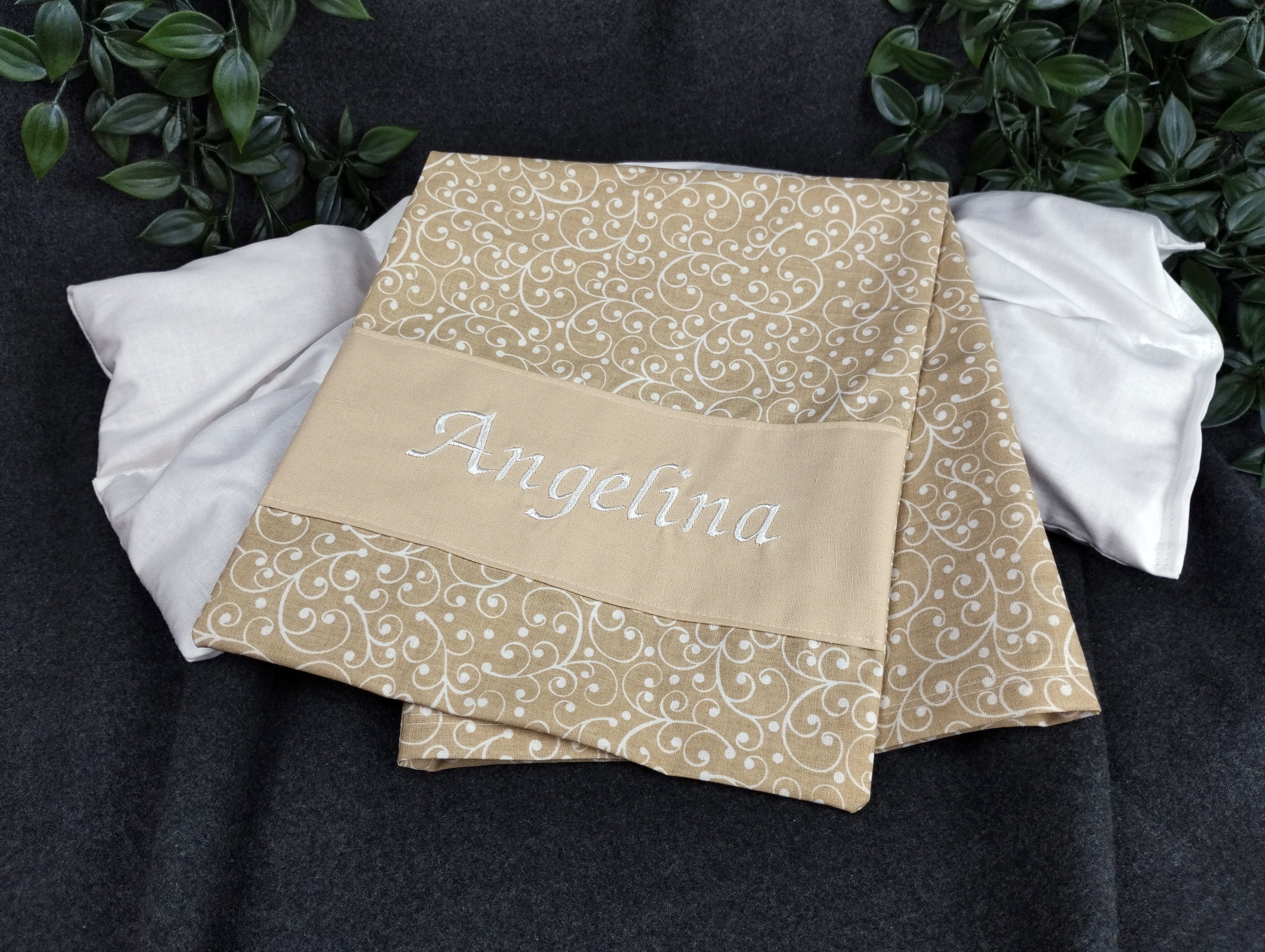 personalisiertes Körnerkissen mit dem Namen Angelina. Das Hauptmotiv in beige mit weißen Ranken und der Name weiß gestickt auf beigem Stoff.