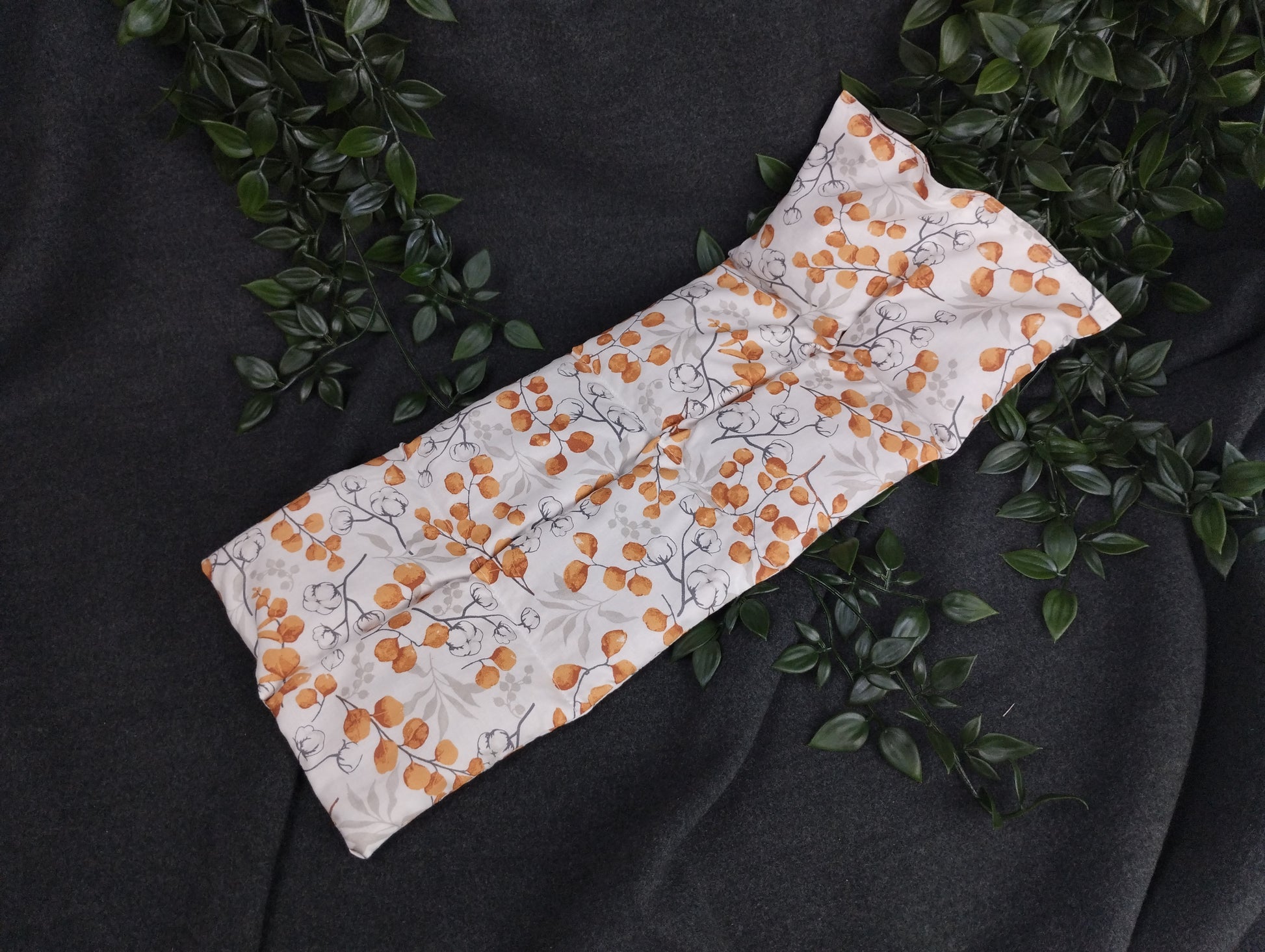 Körnerkissen mit Eucalyptus und Baumwollmotiven auf weißem Hintergrund mit orangenen Akzenten