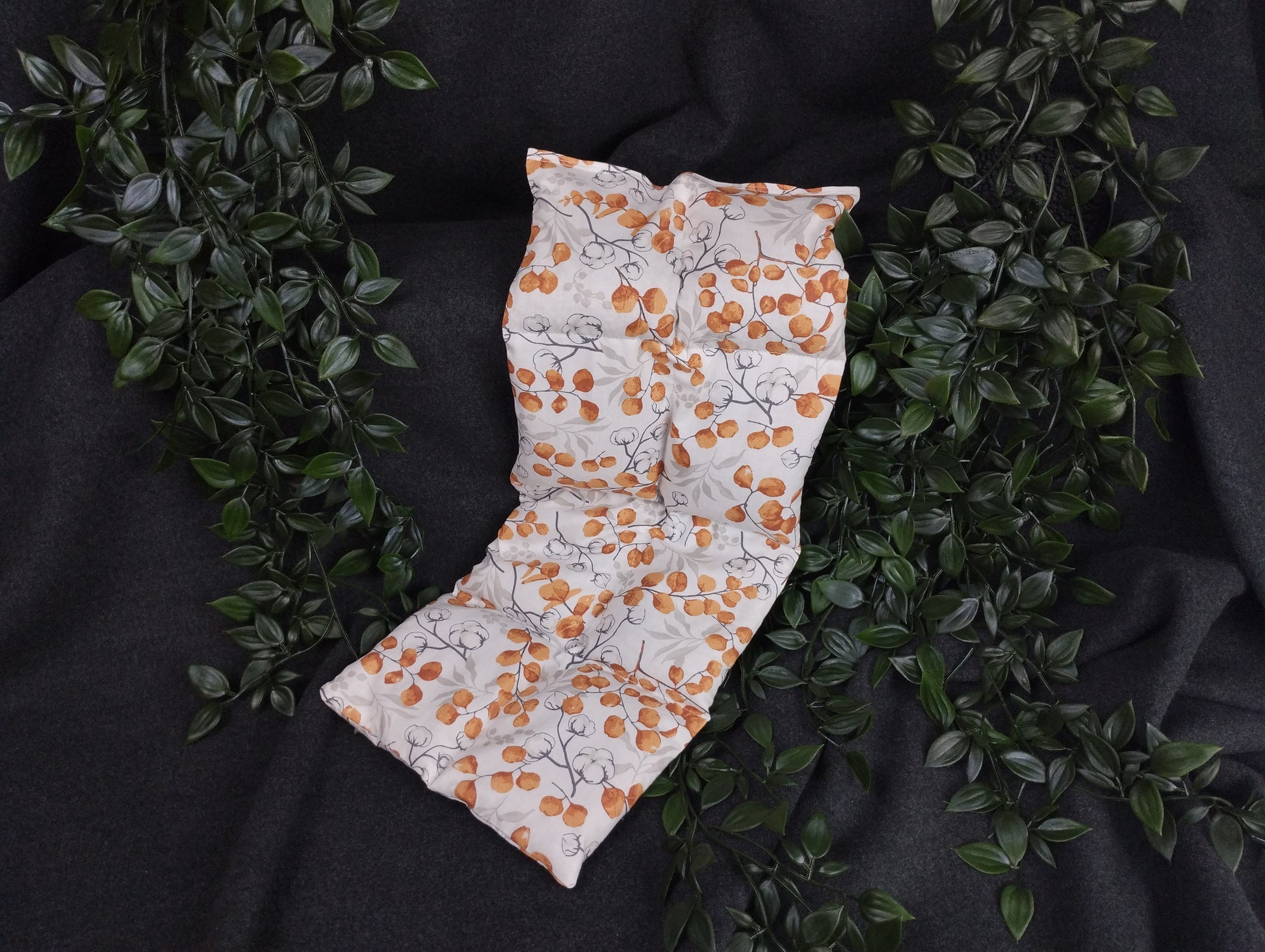 Körnerkissen mit Eucalyptus und Baumwollmotiven auf weißem Hintergrund mit orangenen Akzenten