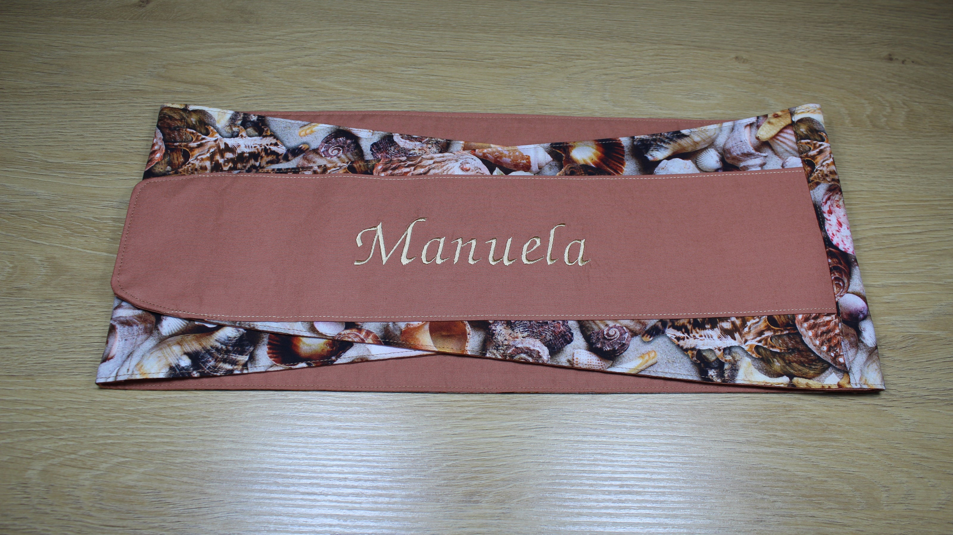 Körnerkissengurt mit Muschelmotiv und dem gestickten Namen Manuela auf braunem Stoff