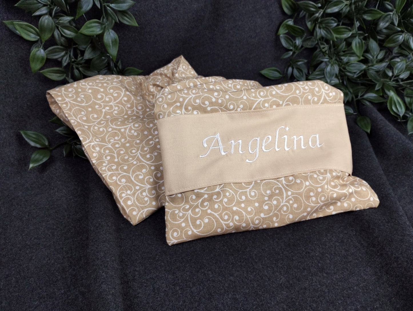 personalisiertes Körnerkissen mit dem Namen Angelina. Das Hauptmotiv in beige mit weißen Ranken und der Name weiß gestickt auf beigem Stoff. 