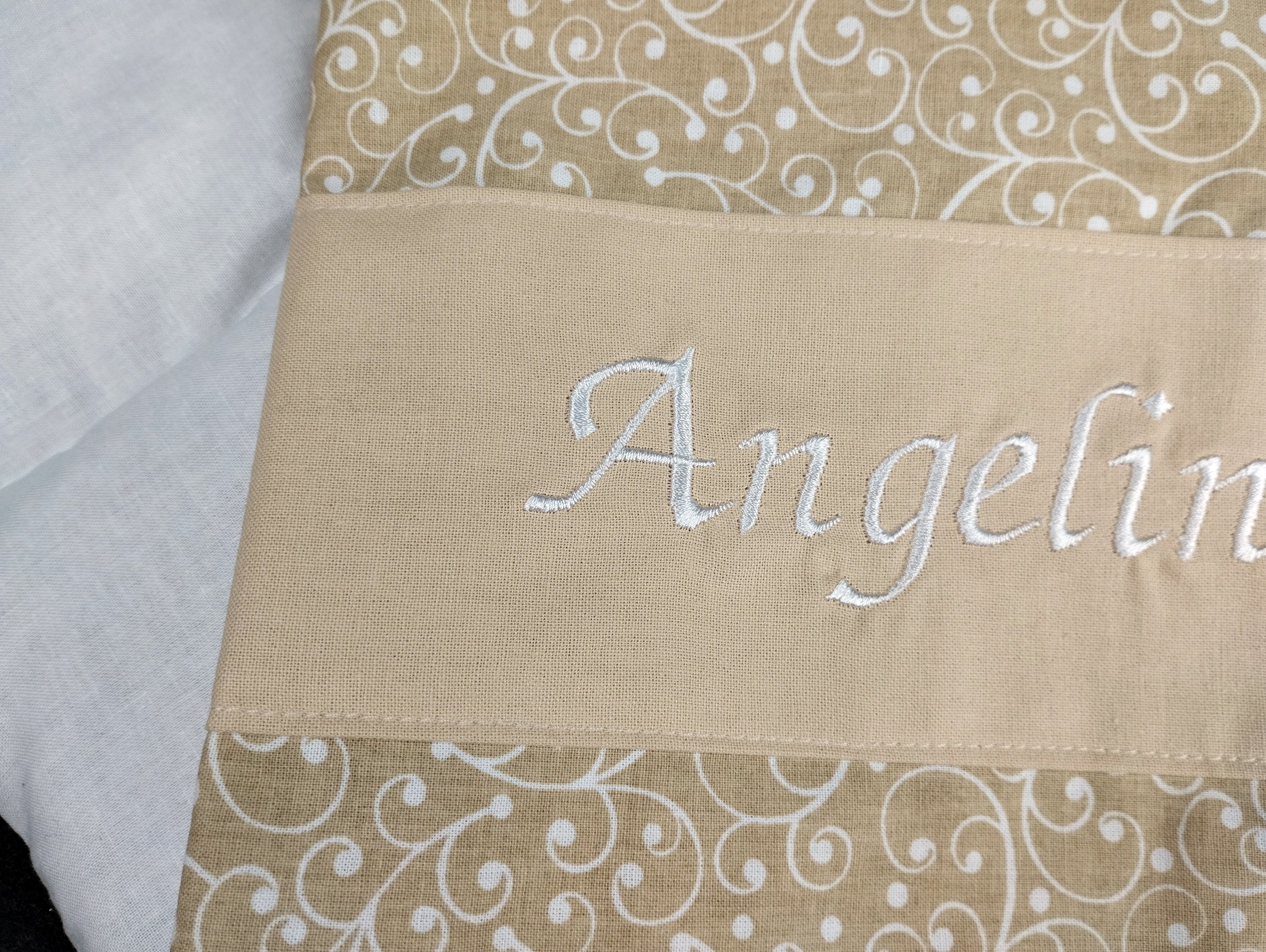 personalisiertes Körnerkissen mit dem Namen Angelina. Das Hauptmotiv in beige mit weißen Ranken und der Name weiß gestickt auf beigem Stoff. 