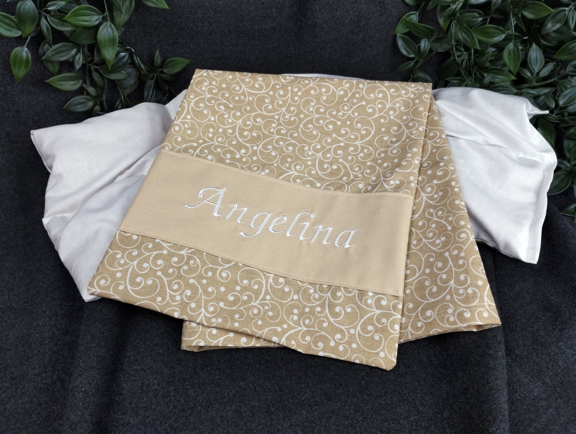personalisiertes Körnerkissen mit dem Namen Angelina. Das Hauptmotiv in beige mit weißen Ranken und der Name weiß gestickt auf beigem Stoff. 