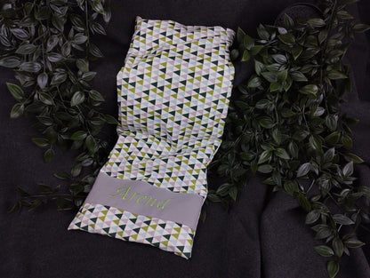 personalisiertes Körnerkissen mit grauen, grünen und türkisfarbenen Dreiecken auf weißem Baumwollstoff. Personalisierung auf grauem Stoff mit grüner Schrift