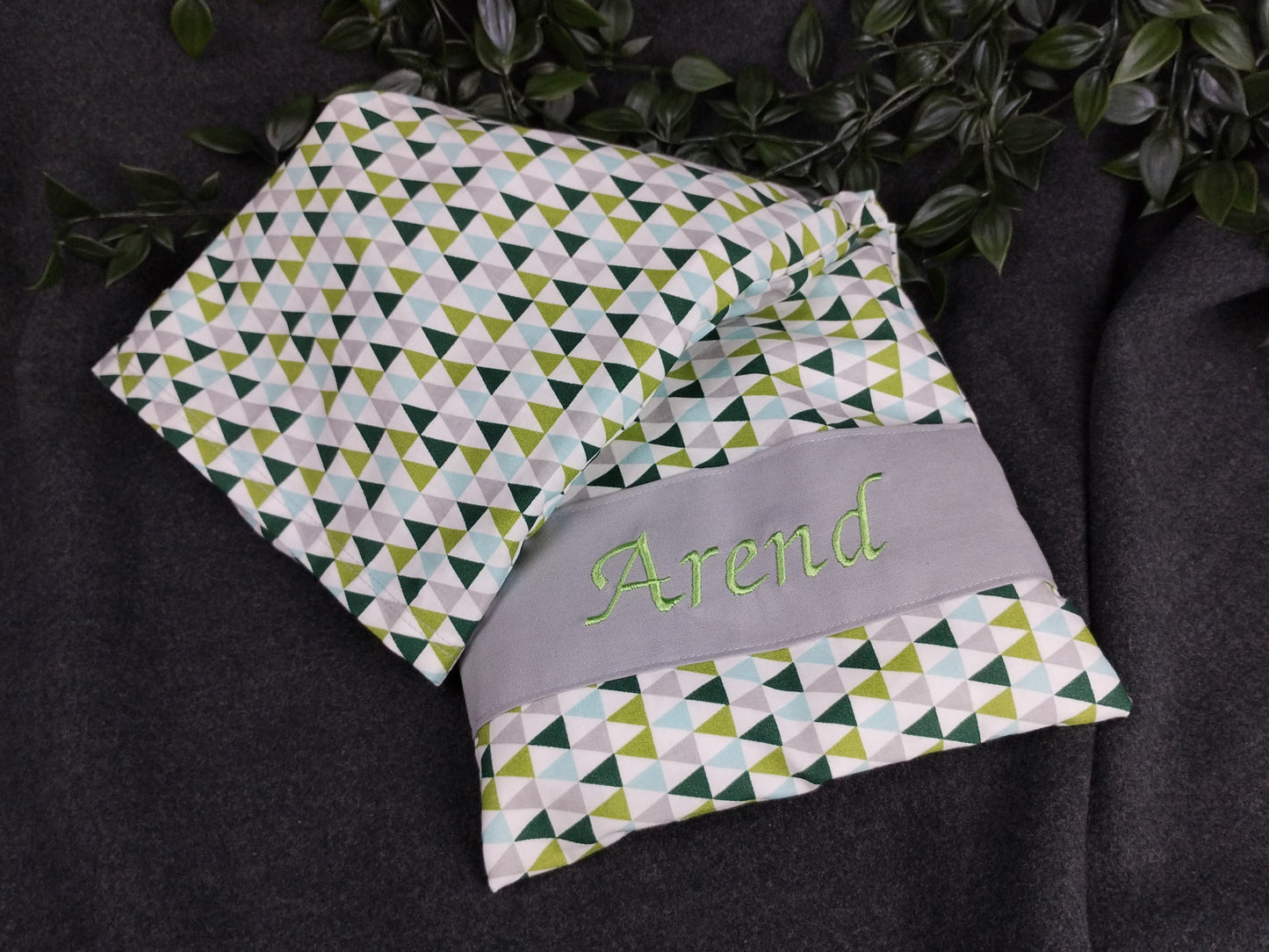 personalisiertes Körnerkissen mit grauen, grünen und türkisfarbenen Dreiecken auf weißem Baumwollstoff. Personalisierung auf grauem Stoff mit grüner Schrift