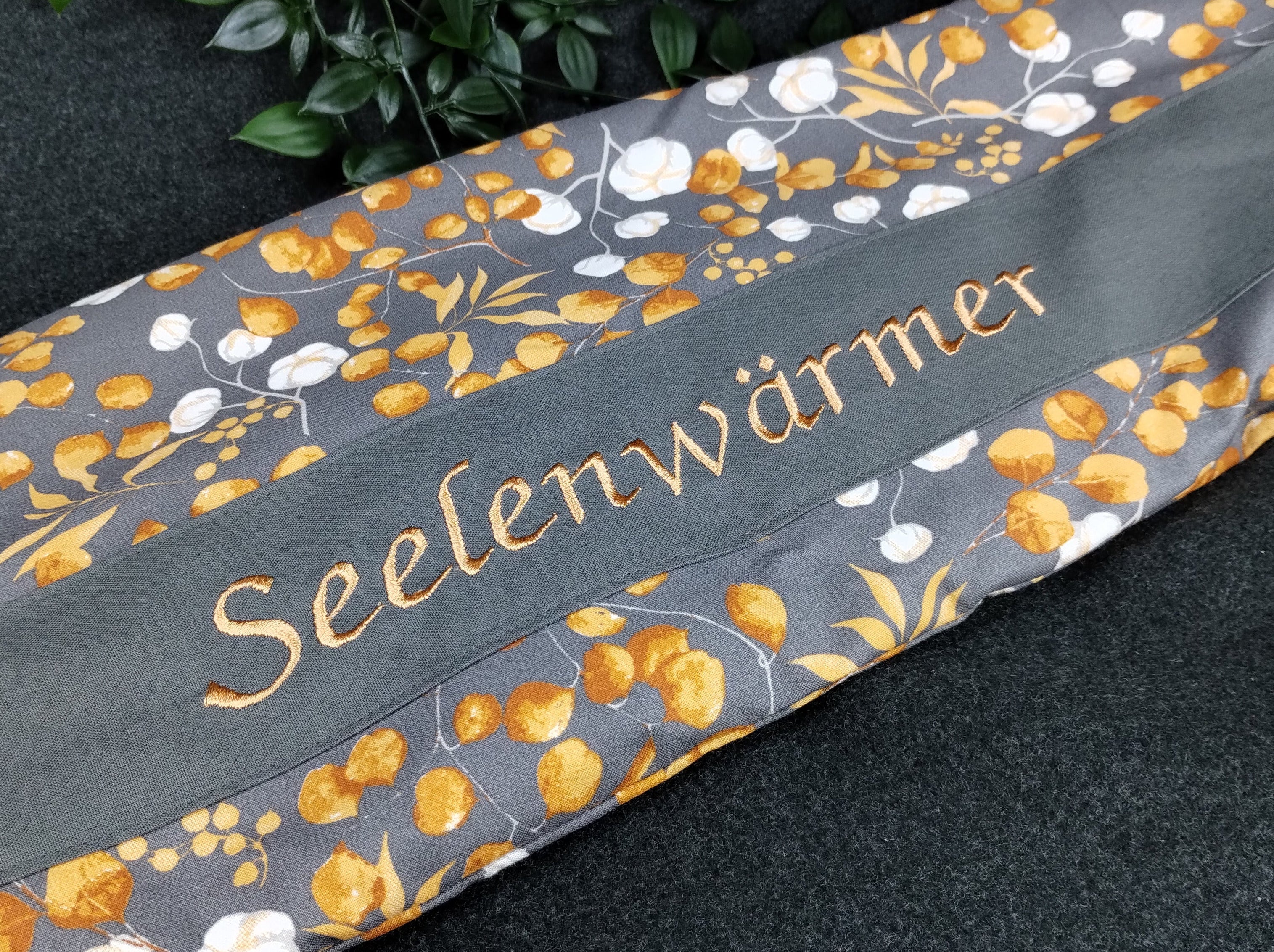 personalisiertes Körnerkissen mit Bezug aus unserem Eucalyptus/Baumwollmotivstoff in grau/orange. Personalisierung auf dunkelgrauem Stoff mit hellorangener Schrift