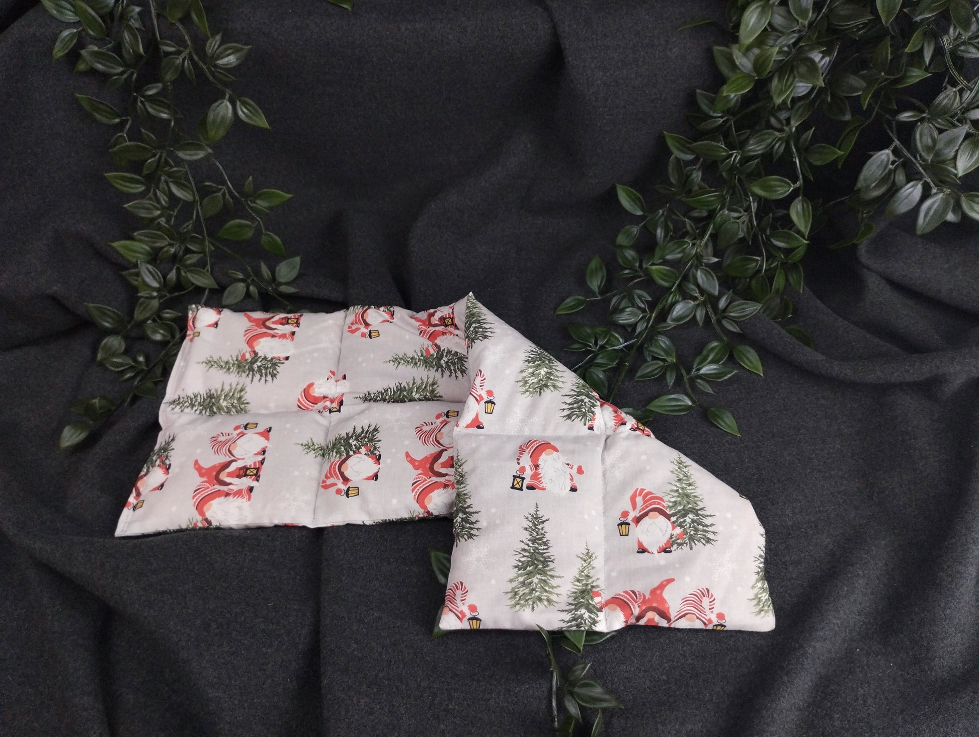 Körnerkissen im weihnachtlichem Look mit Weihnachtsgnomen, die eine Laterne tragen. Verziert wird die graue Landschaft mit grünen Tannenbäumen